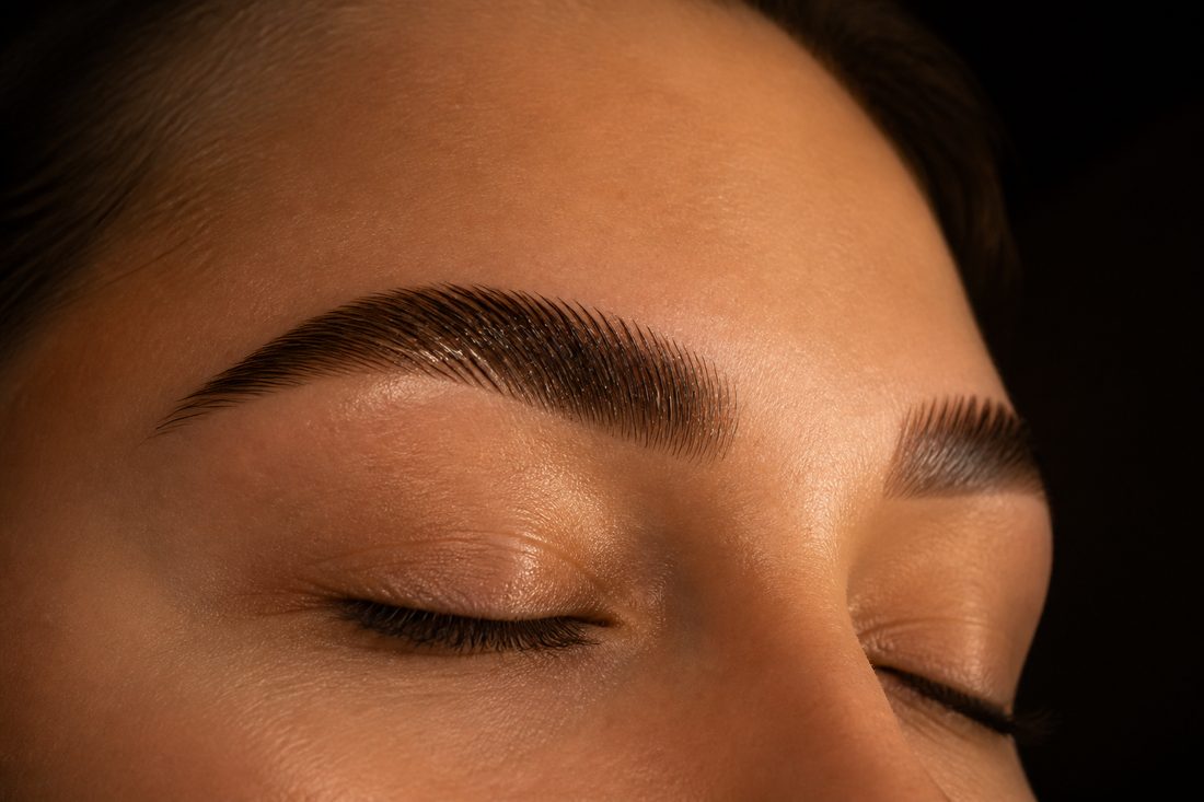 Anonymous close-up of laminated brows in warm gold light — example mood for Aria Brows.